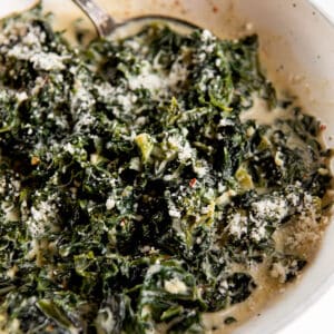 creamed kale with parmesan cheese one top in a bowl with a serving spoon