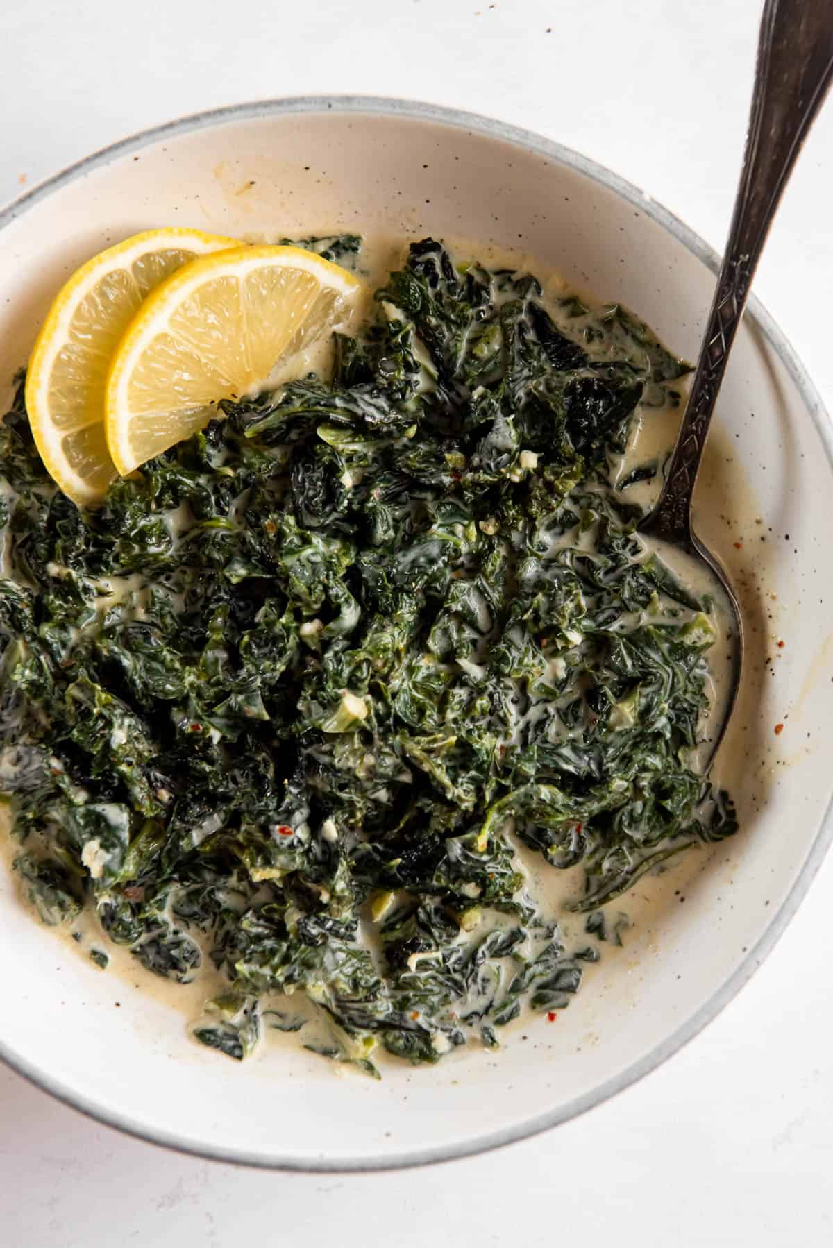 creamed kale in a bowl with two slices of lemon on the side as a garnish