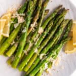 cooked asparagus sitting on a white plate with parmesan cheese on top