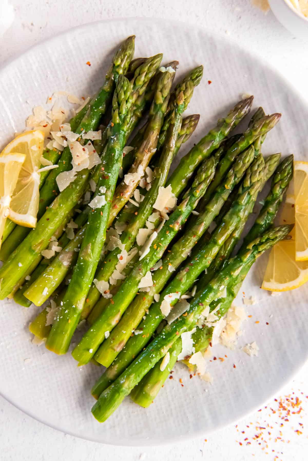 cooked asparagus sitting on a white plate with parmesan cheese on top