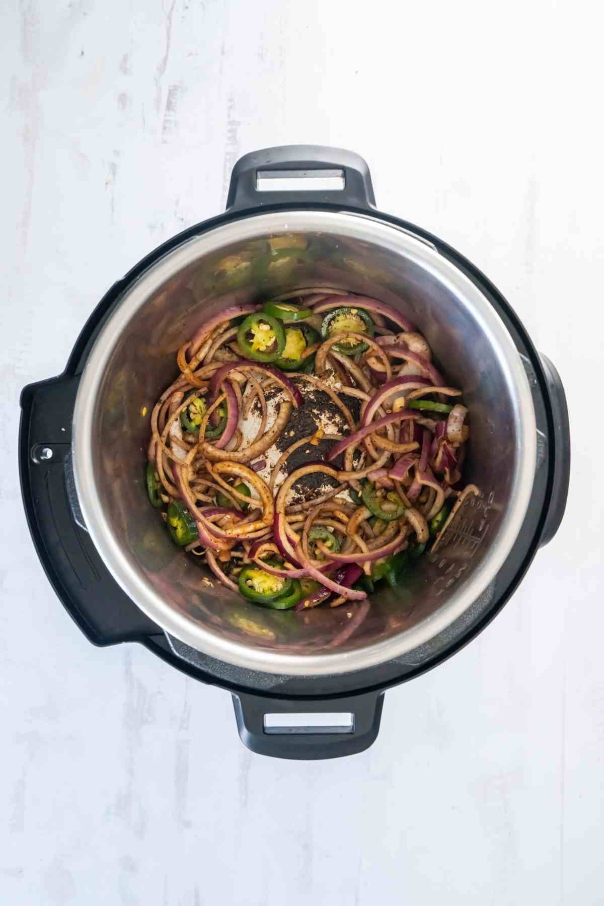 s Sliced onions and jalapeños sautéing in the Instant Pot after the beef is removed.