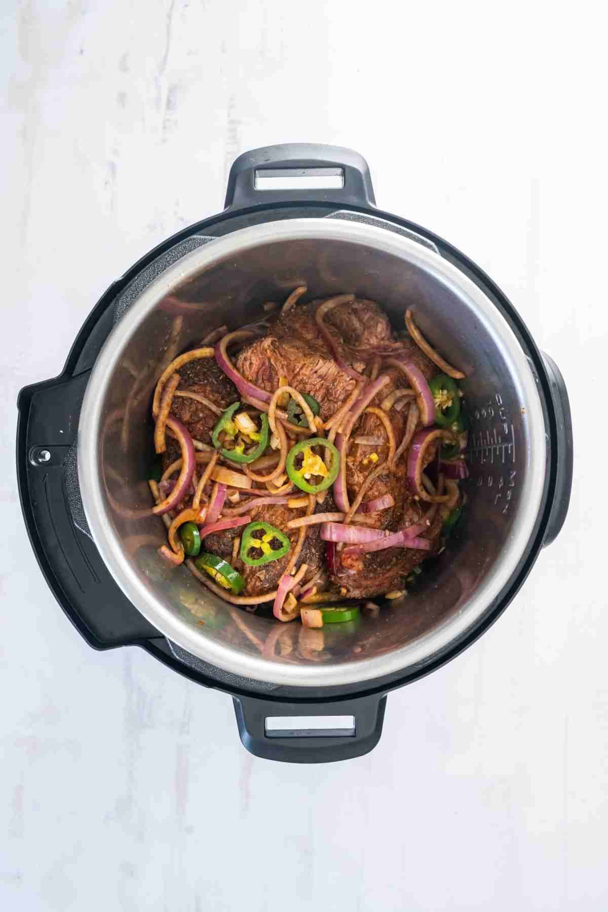 Chuck roast cooking in seasoned broth with onions and jalapeños in the Instant Pot.