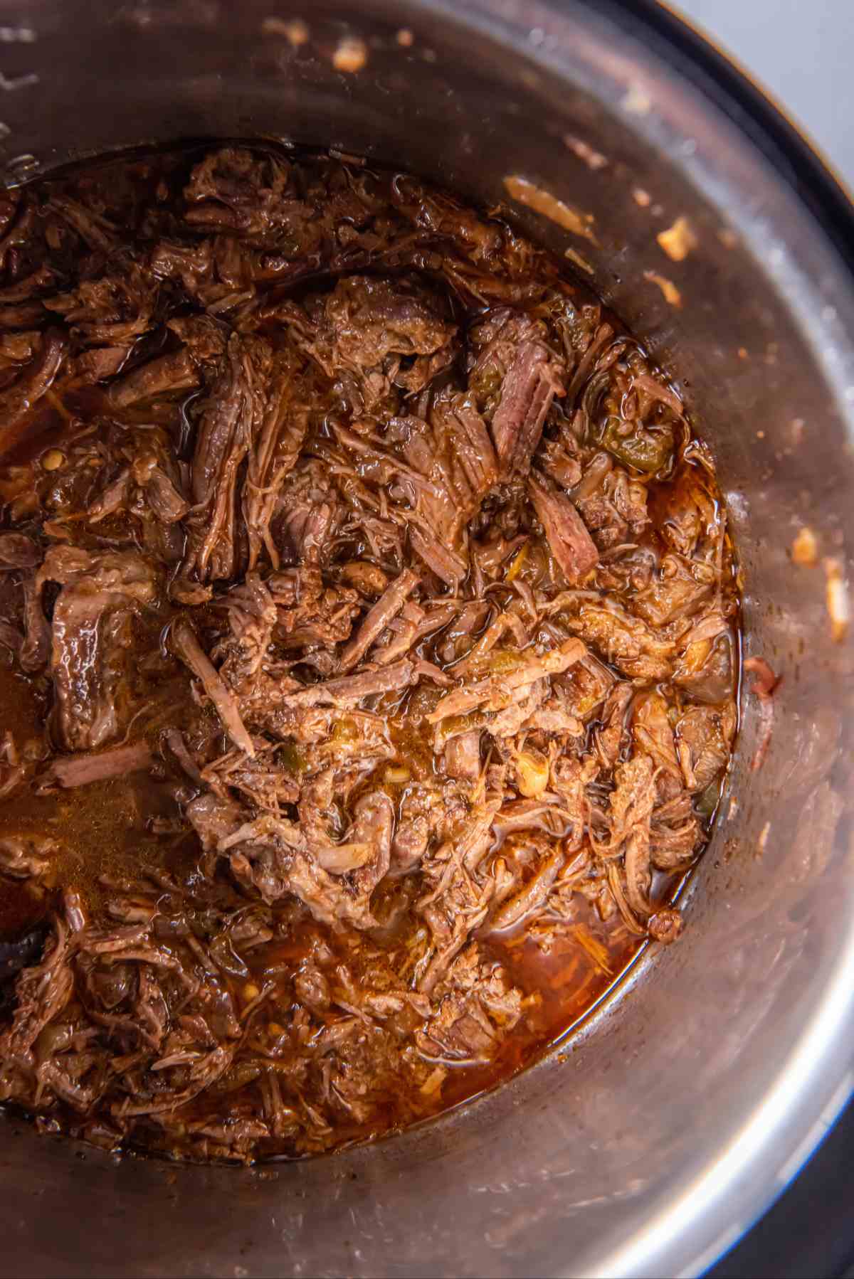 Tender Instant Pot shredded beef mixed with cooking juices, onions, and jalapeños.