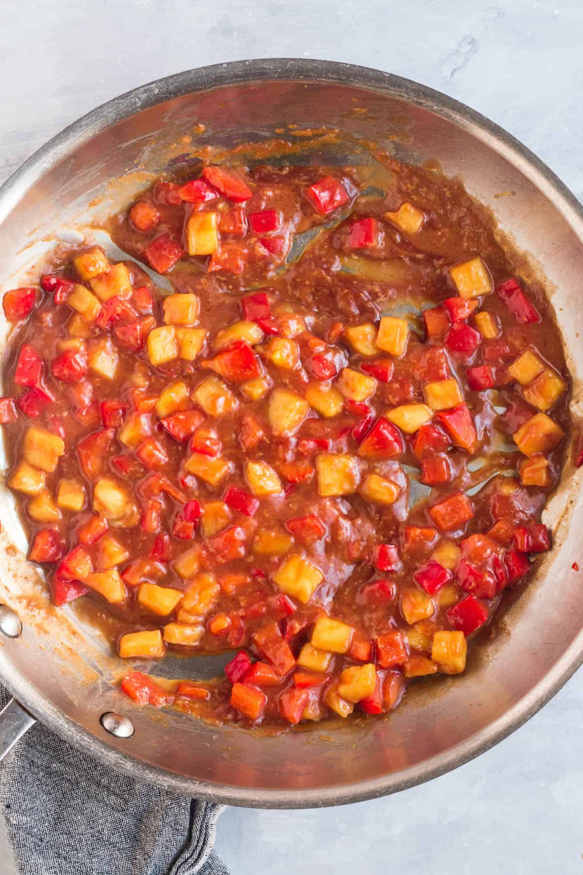 Sweet and sour sauce simmering in a skillet with diced pineapple and red bell pepper.
