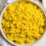 A large white bowl filled with cooked turmeric coconut rice.