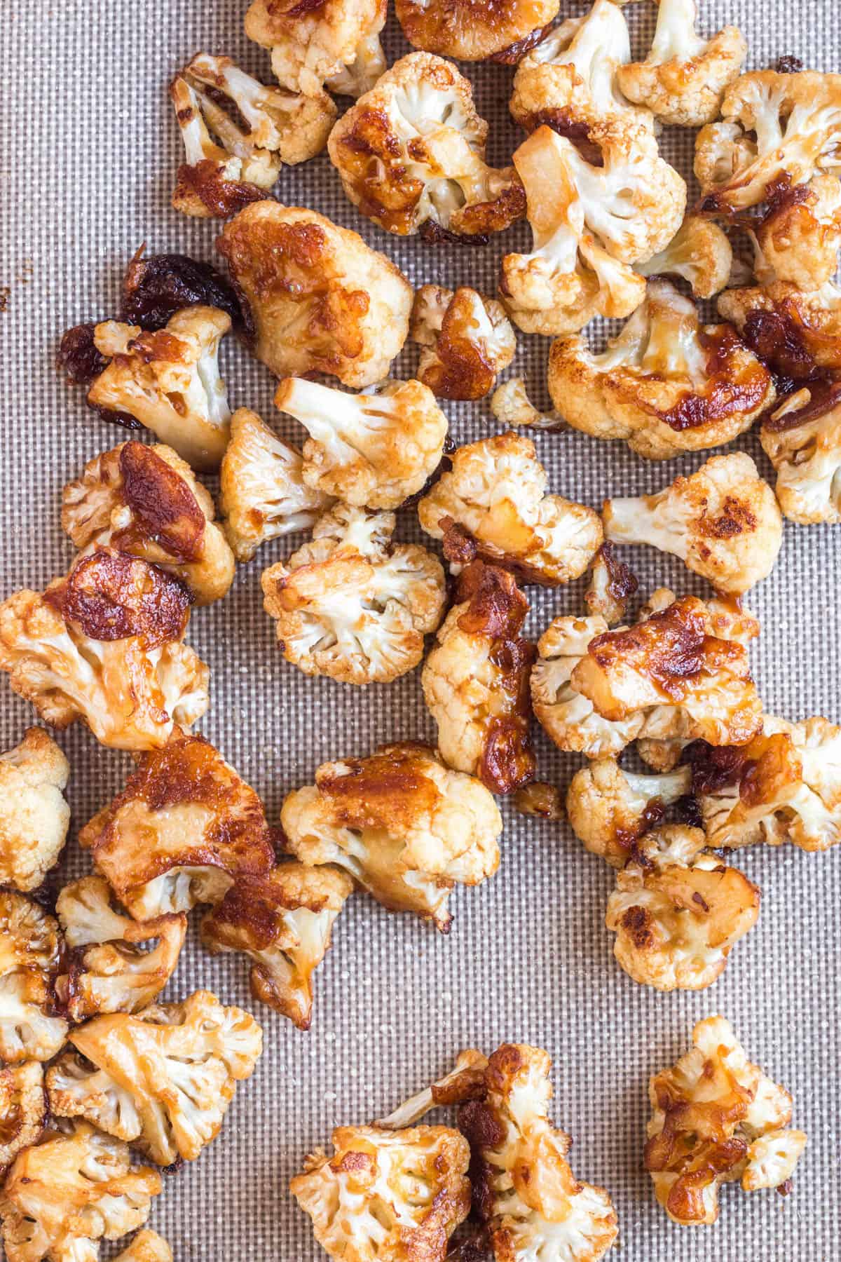 Oven-roasted cauliflower florets with browned, crisp edges spread on a baking sheet.