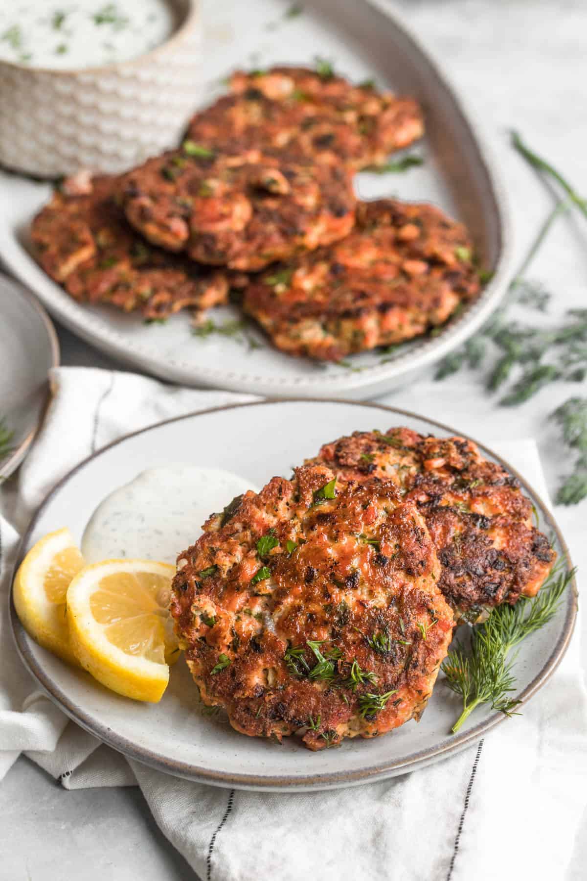 A plate with two salmon patties and a side of tartar sauce.