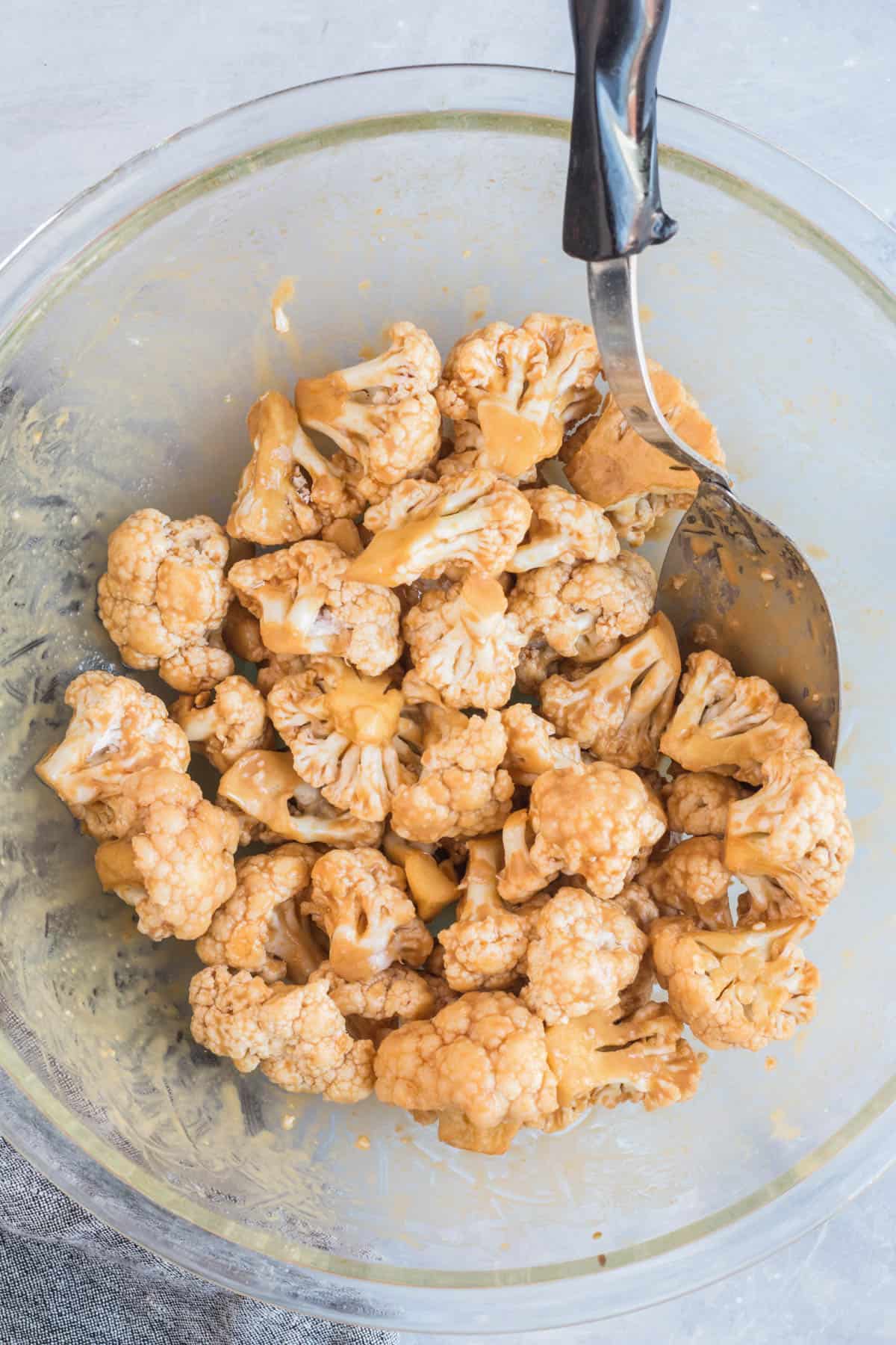 Cauliflower florets coated with seasoning and cornstarch in a mixing bowl before roasting.