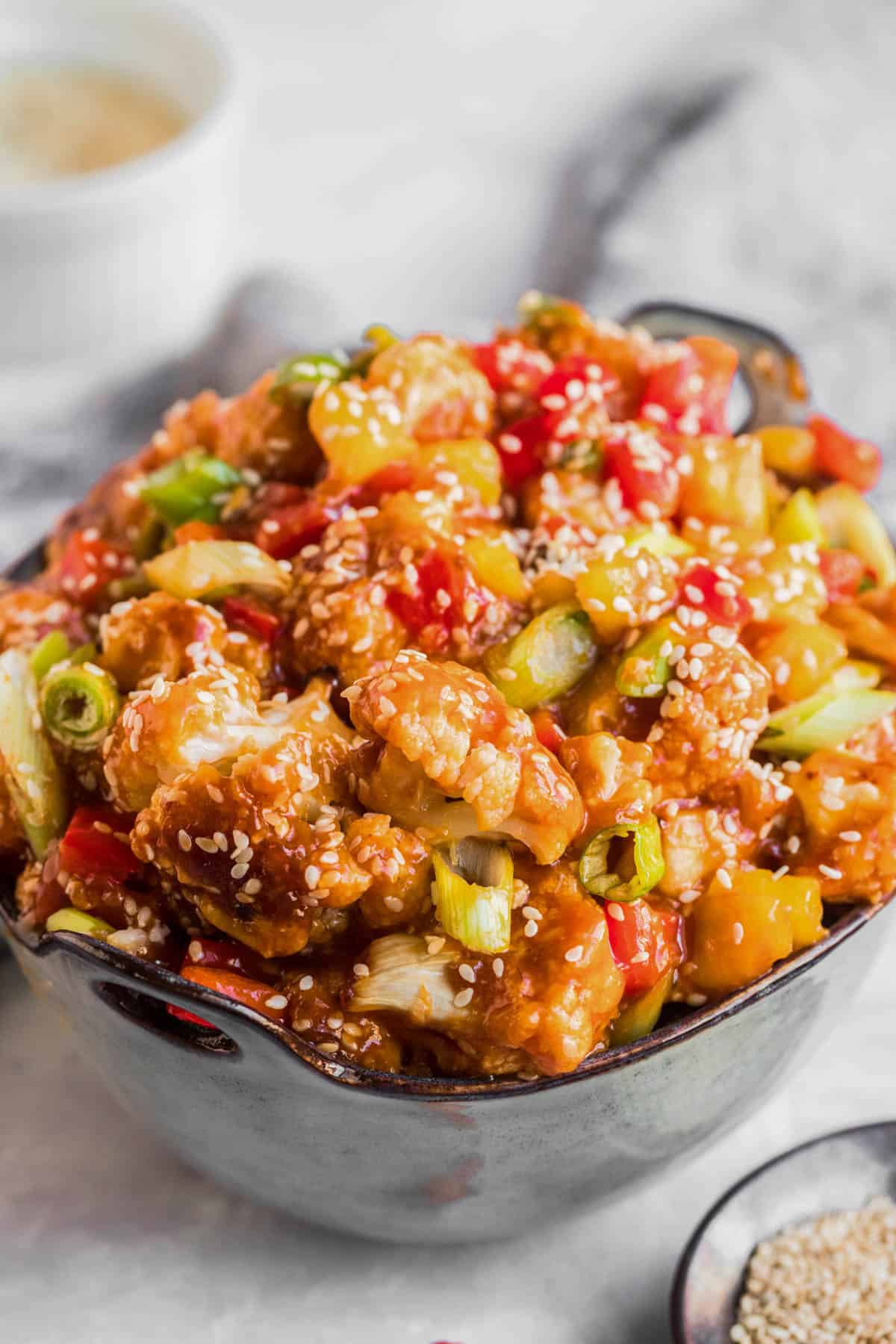 Bowl of sweet and sour cauliflower with pineapple, green onions, and sesame seeds, served hot.