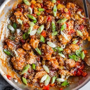sweet and sour cauliflower with sliced green onions and sesame seeds in a skillet
