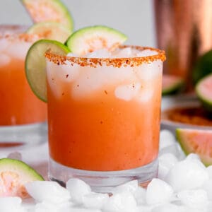 One guava margarita sitting on a white countertop with slices of lime as garnish.