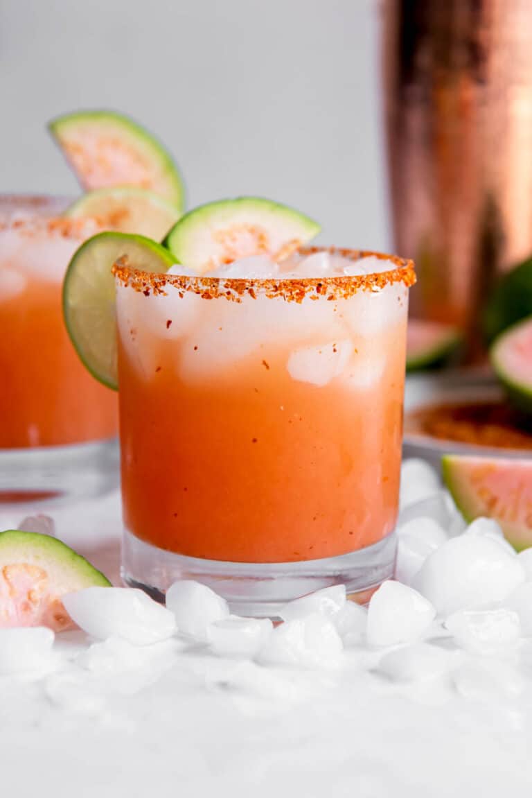 One guava margarita sitting on a white countertop with slices of lime as garnish.