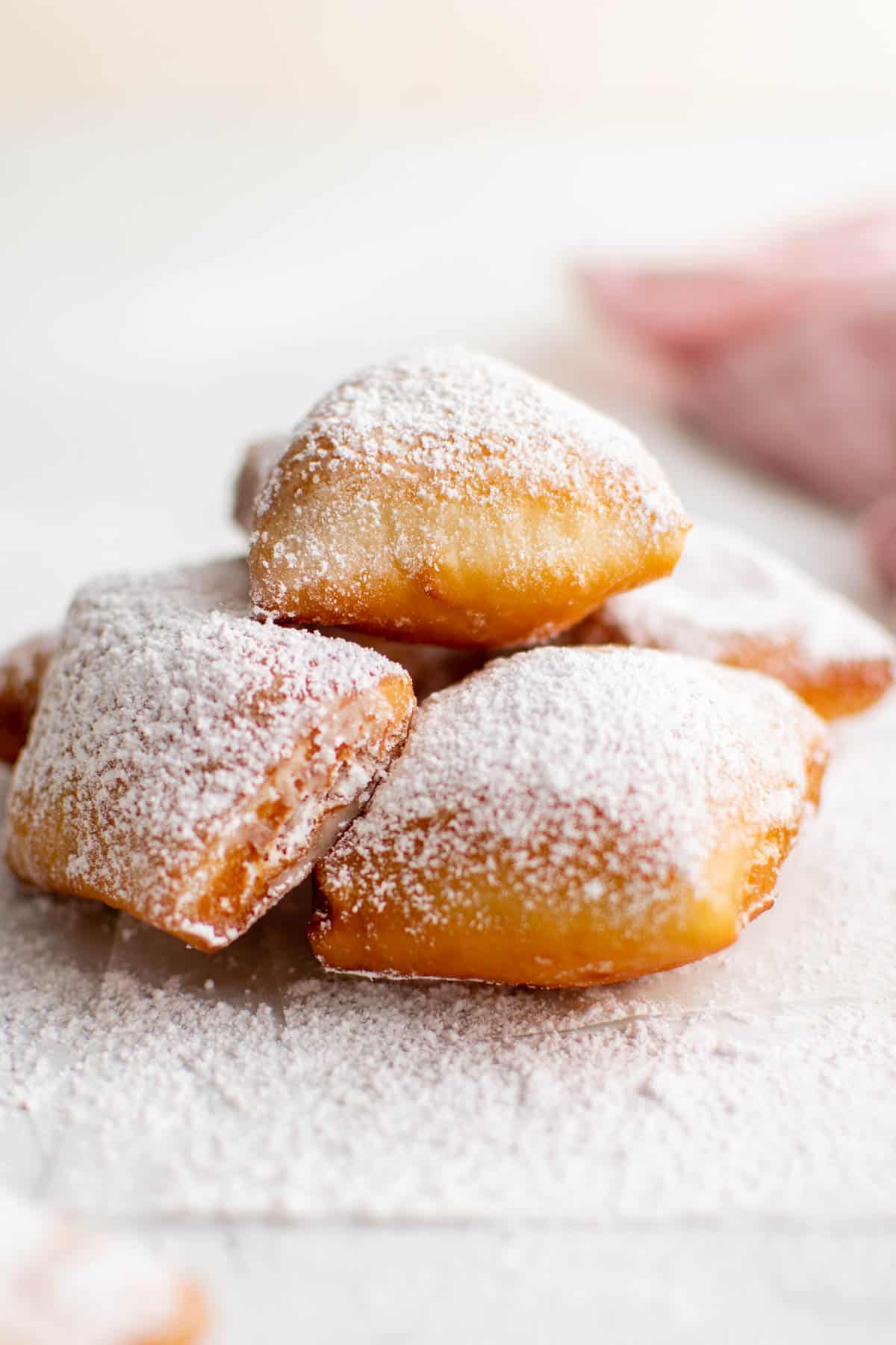 A pile of beignets dusted with powdered sugar sitting on a white countertop.