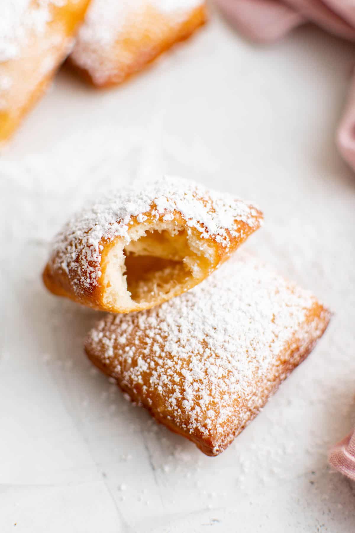 A bite taken out of a beignet that is sitting next to another beignet on a counter.
