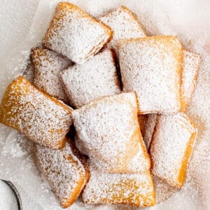 A large pile of sugar dusted beignets sitting on a piece of parchment paper.