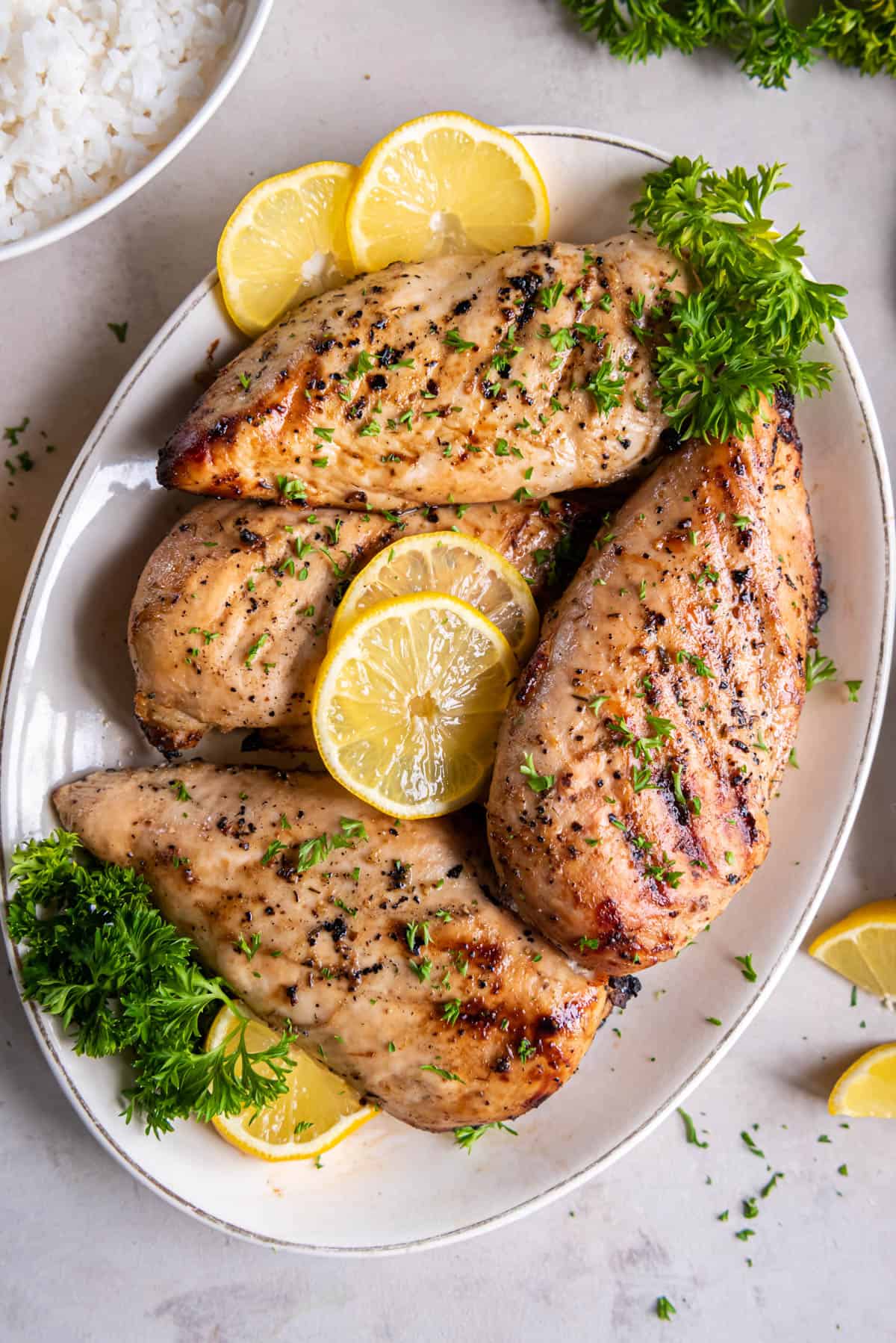 A white plate topped with grilled lemon pepper chicken and garnished with lemon slices and fresh parsley.