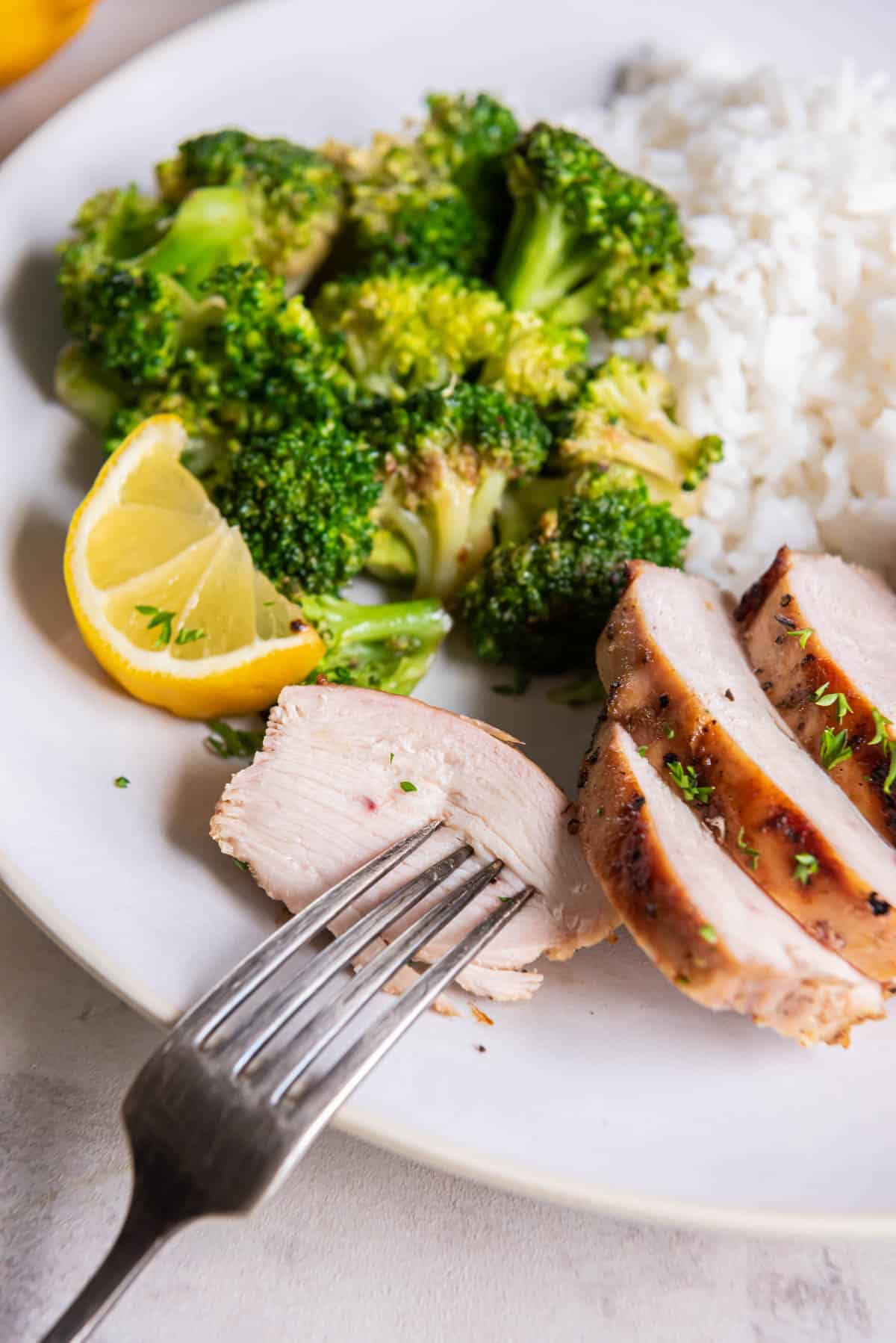 Sliced pieces of grilled lemon pepper chicken on a plate with broccoli.
