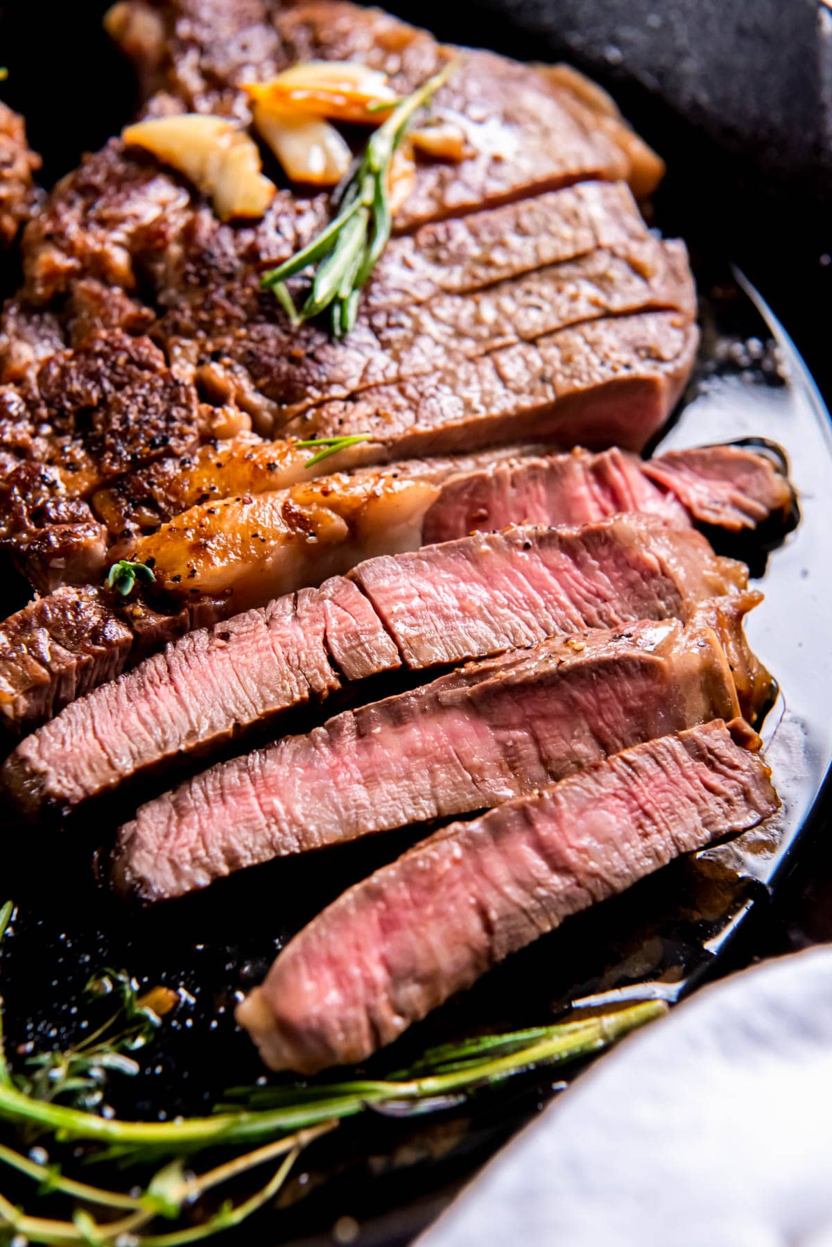 A cooked ribeye steak sliced in a cast iron pan for serving.