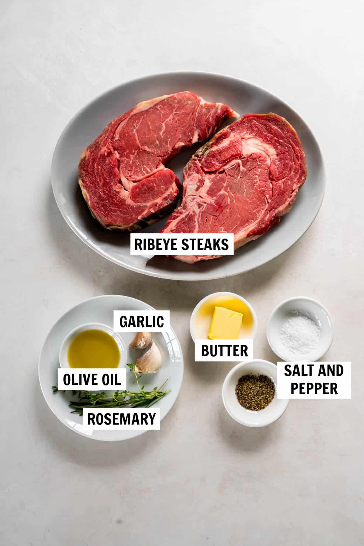 All of the ingredients for pan seared ribeye steaks in bowls on a white countertop.