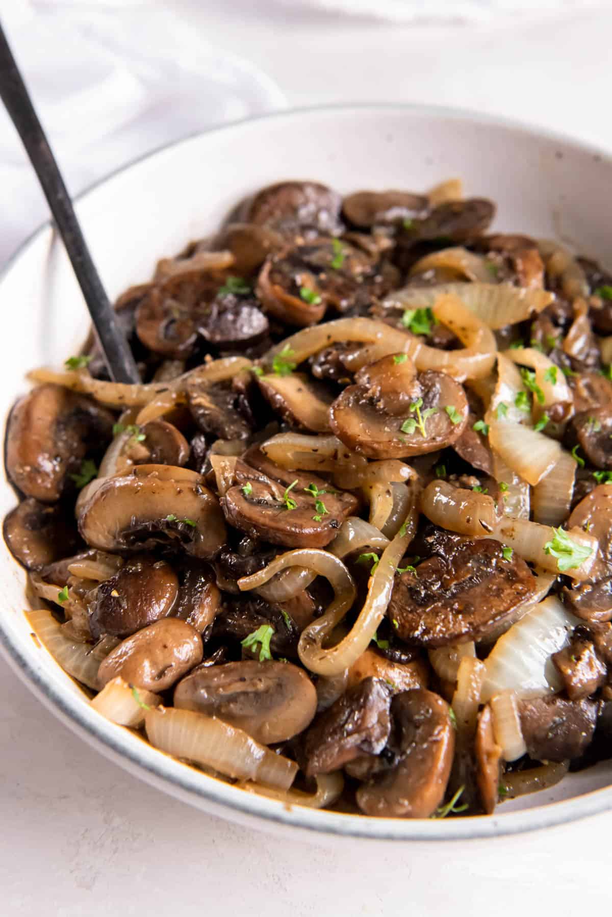 Sautéed mushrooms and onions in a white bowl on a white tabletop.