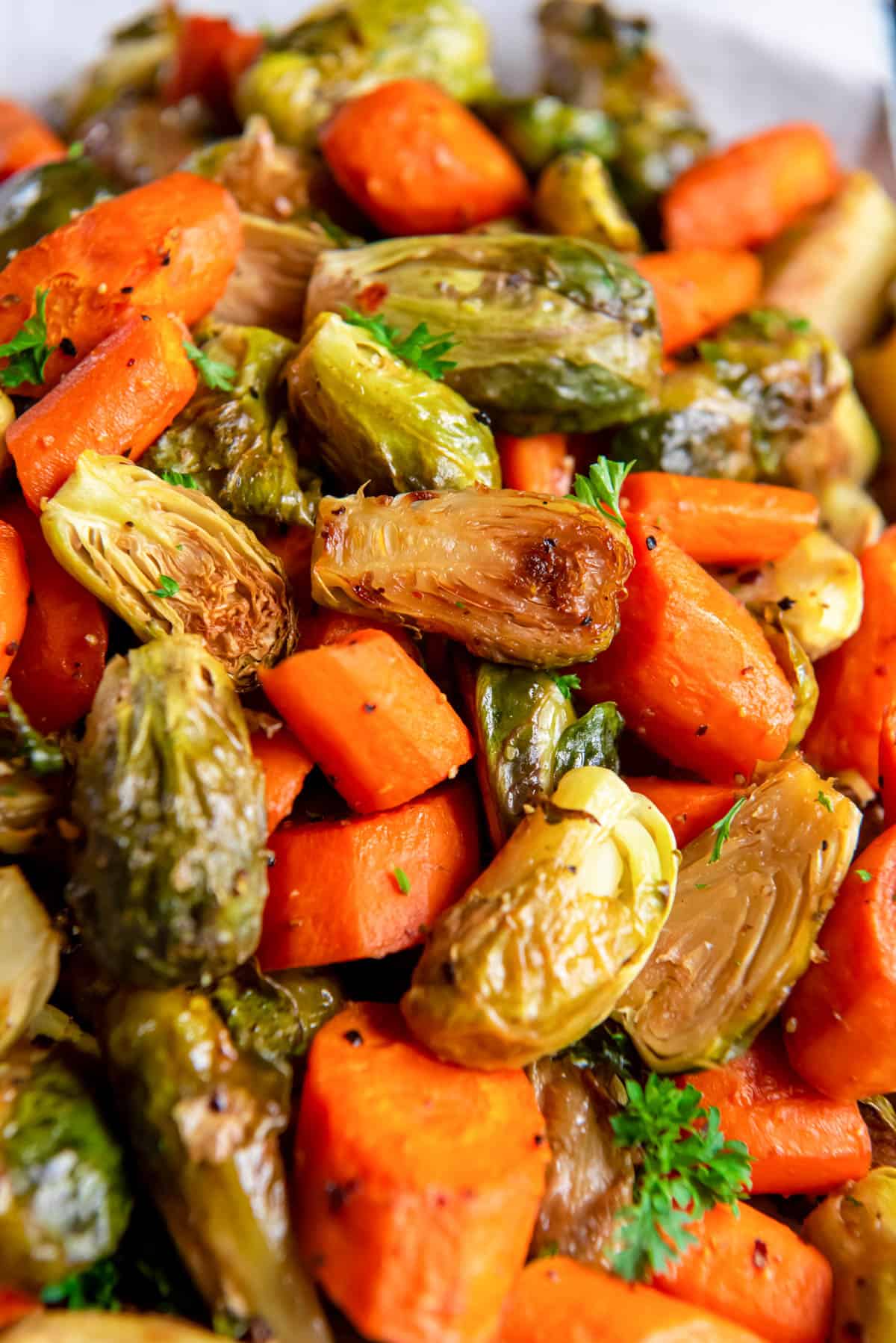 A close up photo of the roasted brussels sprouts and carrots in a bowl garnished with fresh parsley.