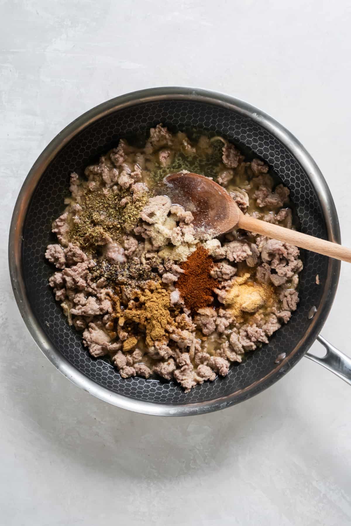Cooked ground turkey in a pan with the seasonings sprinkled on top before mixing together.