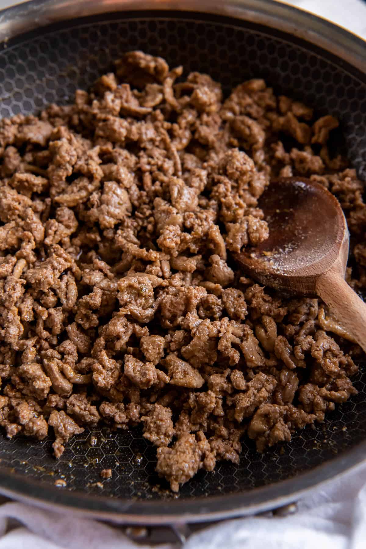 Cooked seasoned ground beef in a skillet with a wooden spoon.