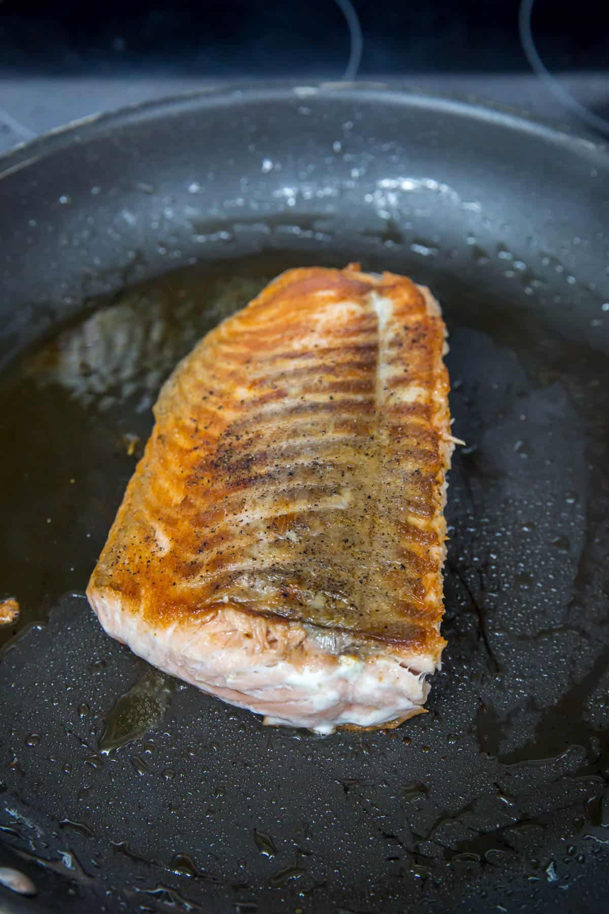 A salmon filet cooking in a nonstick skillet.