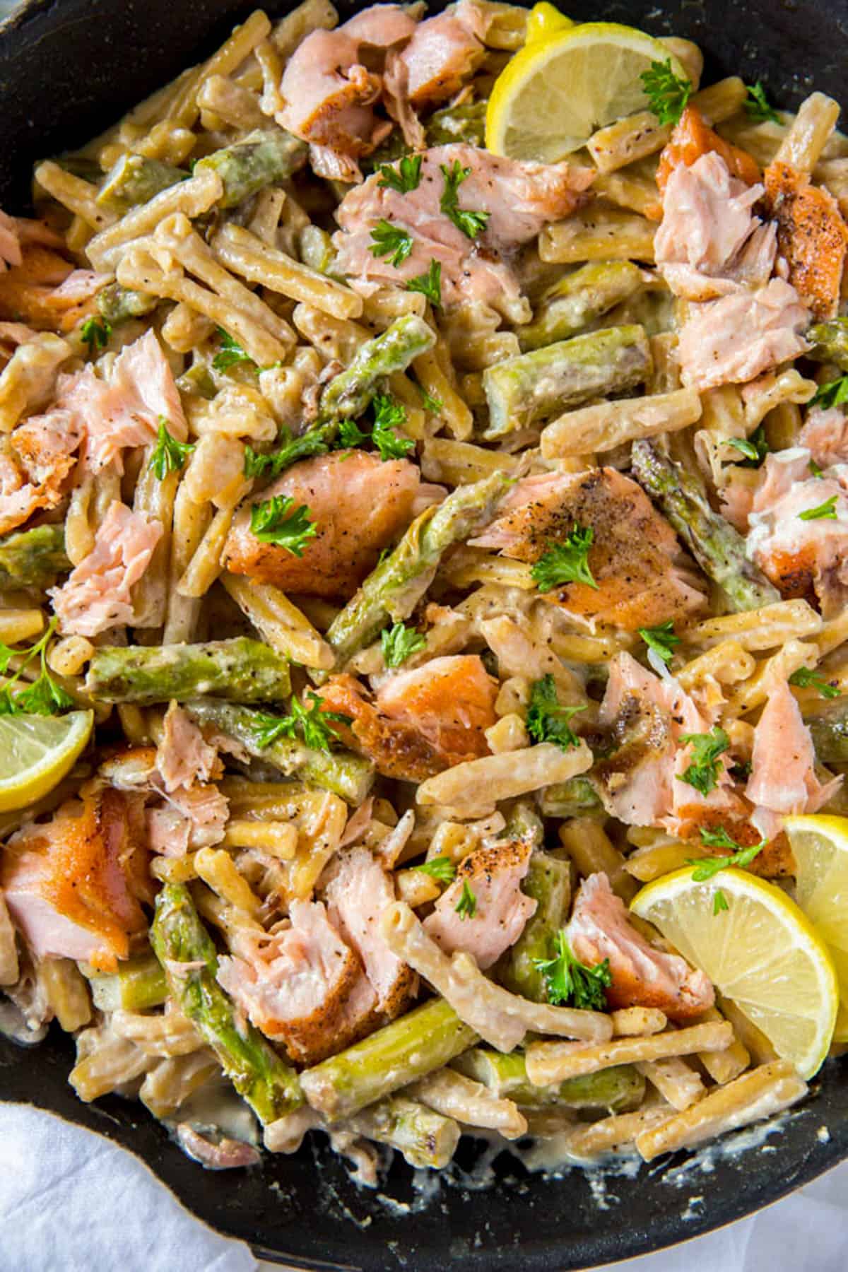 Cooked pasta with salmon, asparagus and a creamy lemon sauce in a skillet ready for serving. Freshly chopped parsley is garnished on top.