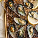 Baked mussels in garlic butter on a sheet pan with tongs for serving,