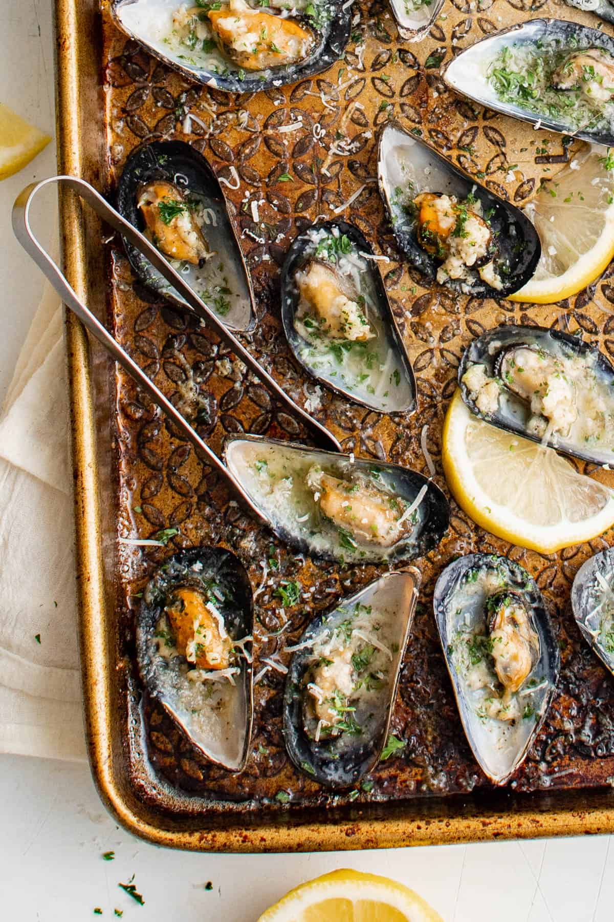 Baked mussels in garlic butter on a sheet pan with tongs for serving,