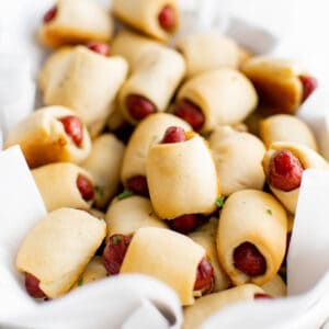 A large pile of pigs in a blanket appetizer in a large white bowl.