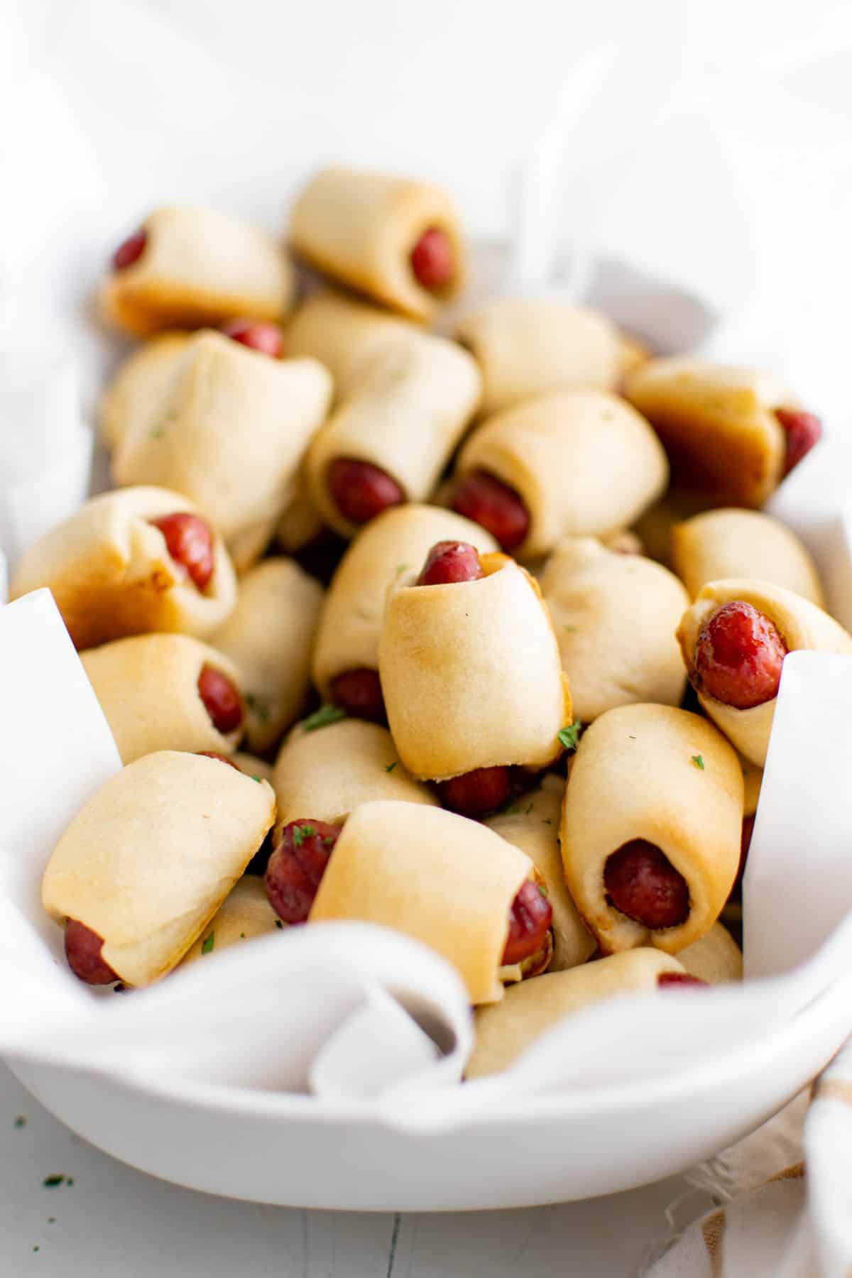 A large pile of pigs in a blanket appetizer in a large white bowl.