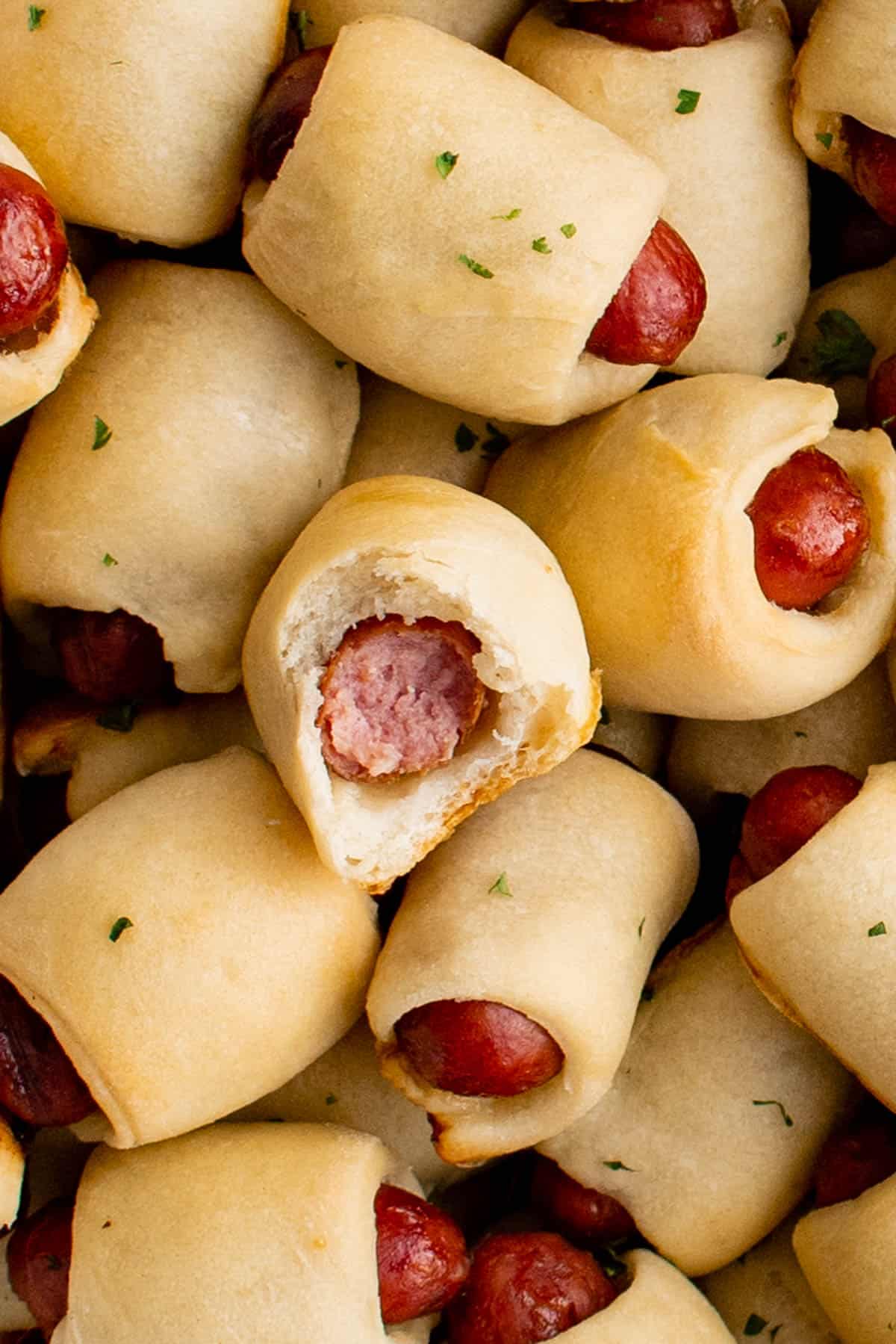 Close up photo of pigs in a blanket. One has a bite taken out of it so you can see the inside. 