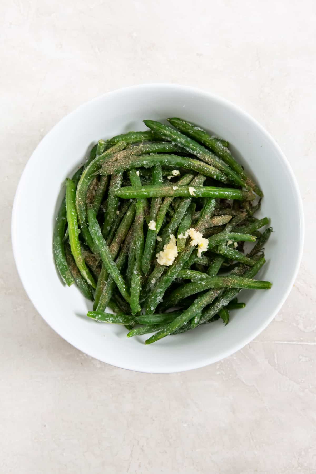 Green beans, garlic, olive oil, salt and pepper in a white bowl before mixing to combine.