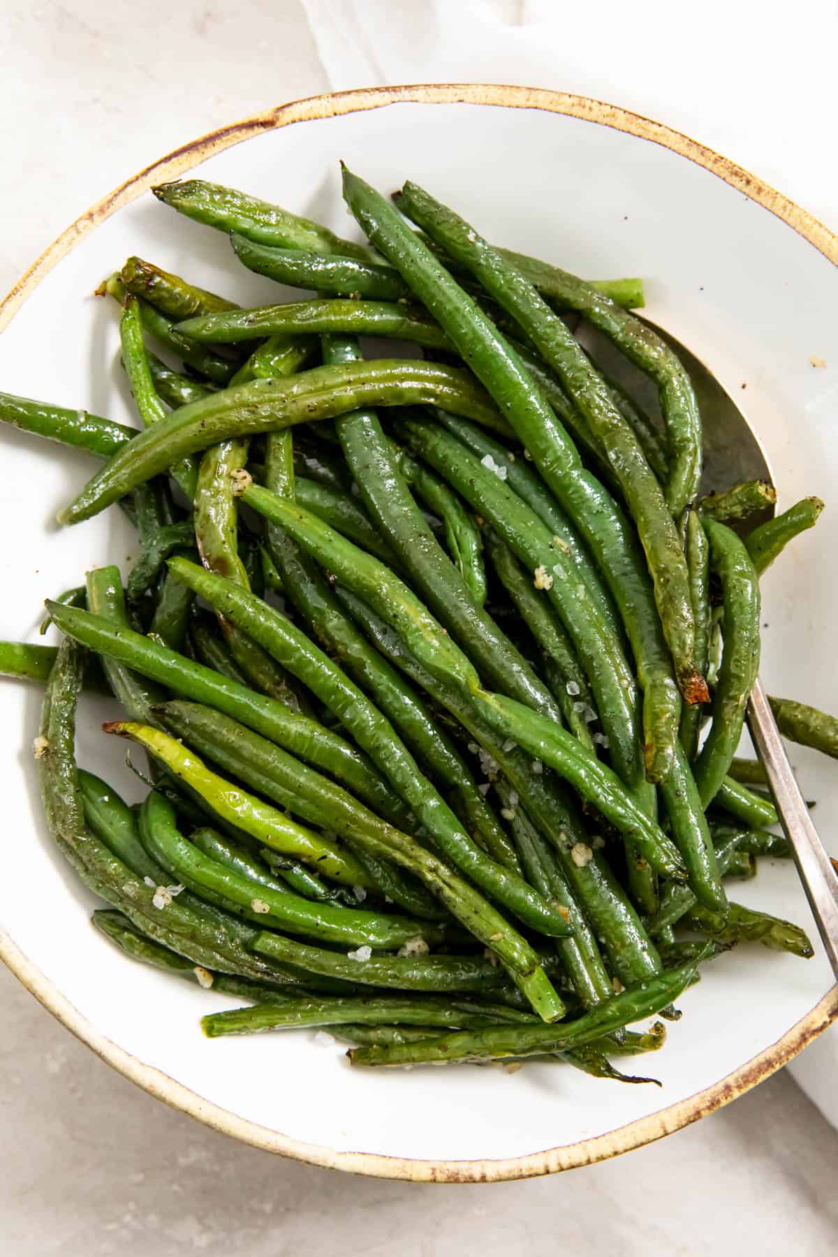 Cooked air fryer green beans sitting in a white bowl with a spoon for serving.
