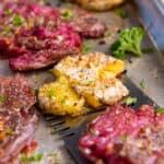 A spatula picks up smashed fingerling potatoes off of a baking sheet after baking in the oven.