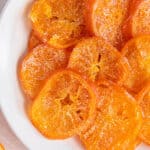 Candied orange slices piled on top of a white plate in a circle pattern.