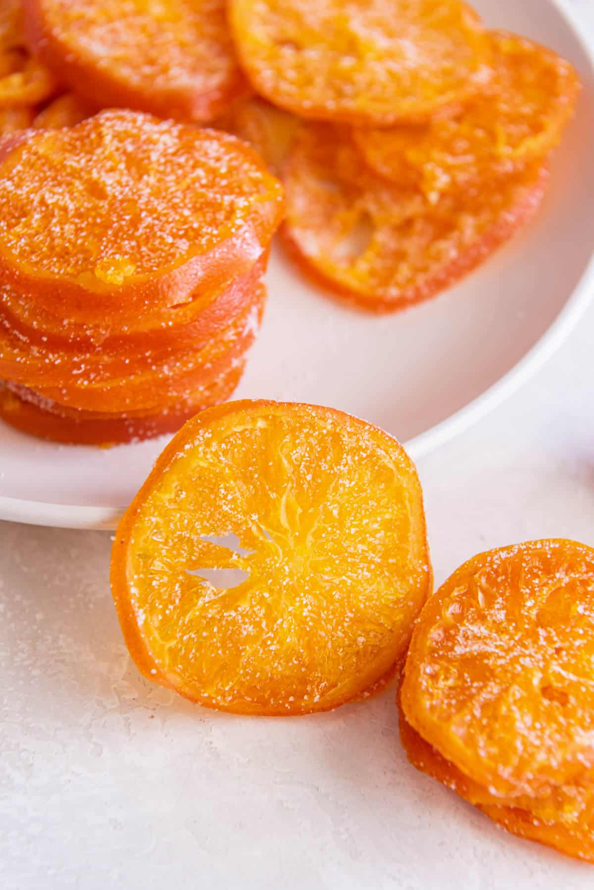Candied orange slices sitting on a white plate with one candied orange peel sitting propped up in front of the plate.