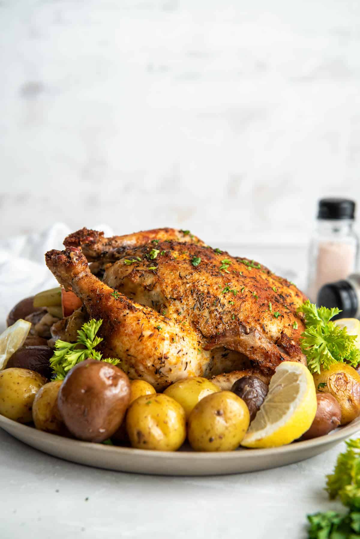 The roasted whole chicken sitting on a white plate with the cooked potatoes.