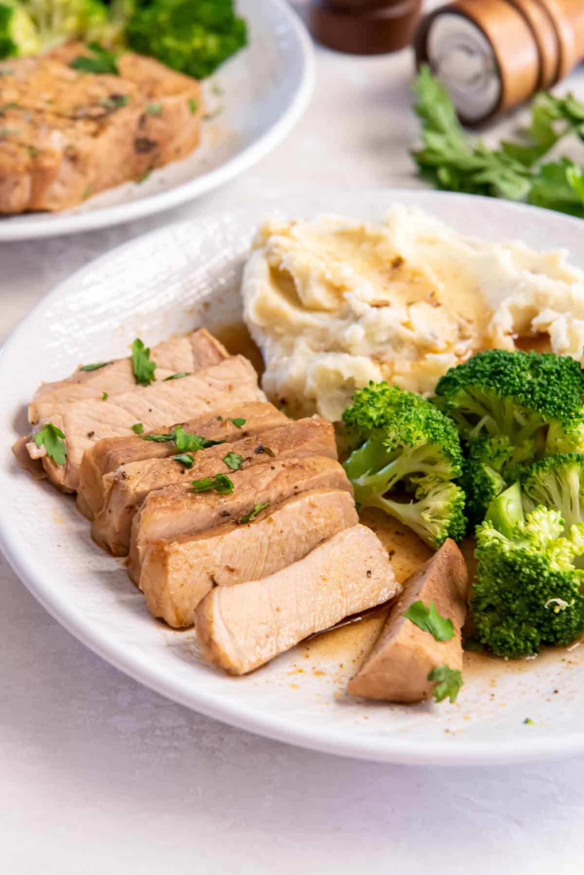 A cooked pork chop sliced into many pieces and served on a plate with cooked broccoli and mashed potatoes.