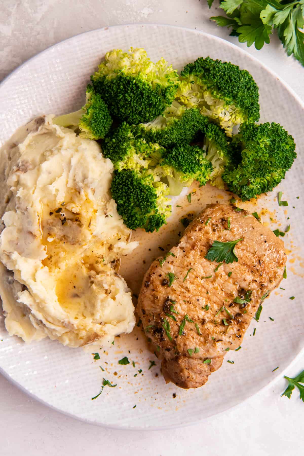 A white plate with a cooked boneless pork chop, steamed broccoli and mashed potatoes with gravy.