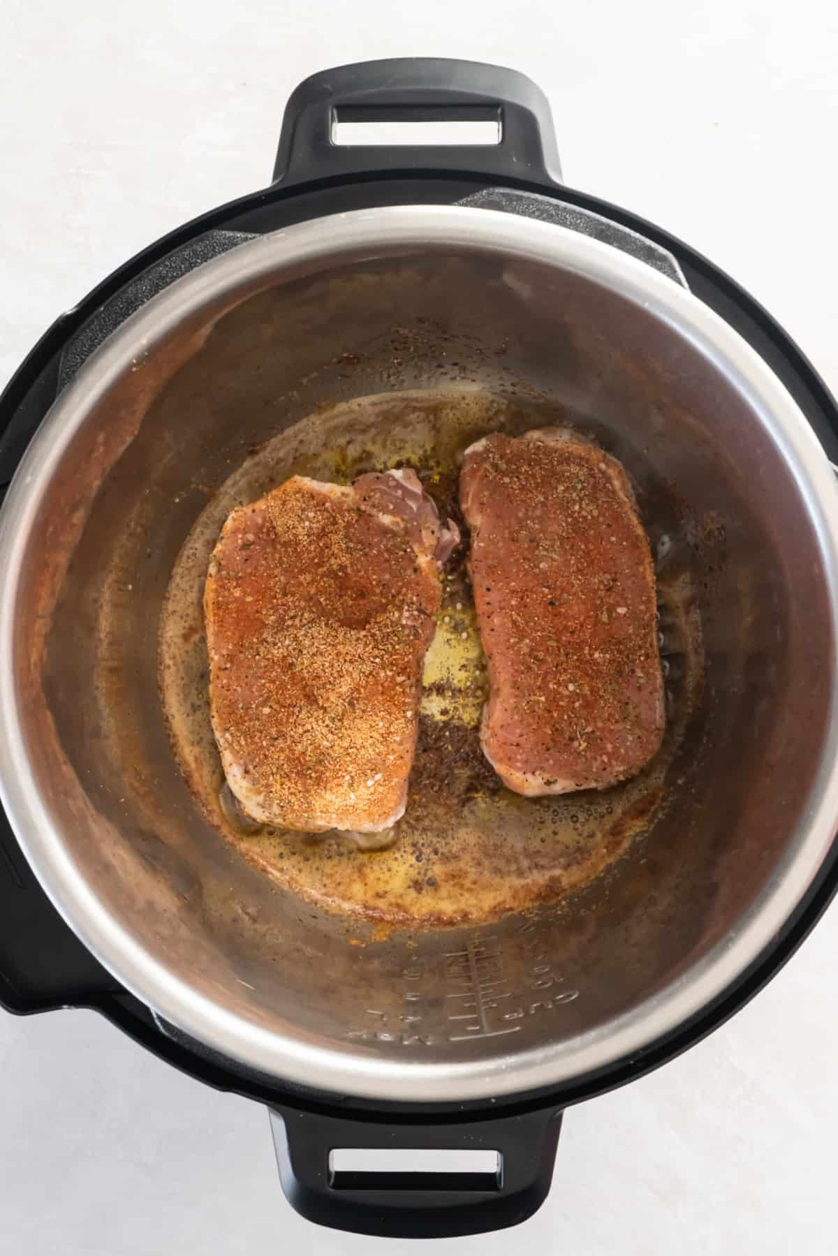 Two pork seasoned pork chops being seared in an instant pot.