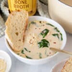 A bowl of chicken florentine soup sitting on a white countertop with a jar of zoup chicken bone broth in the background.