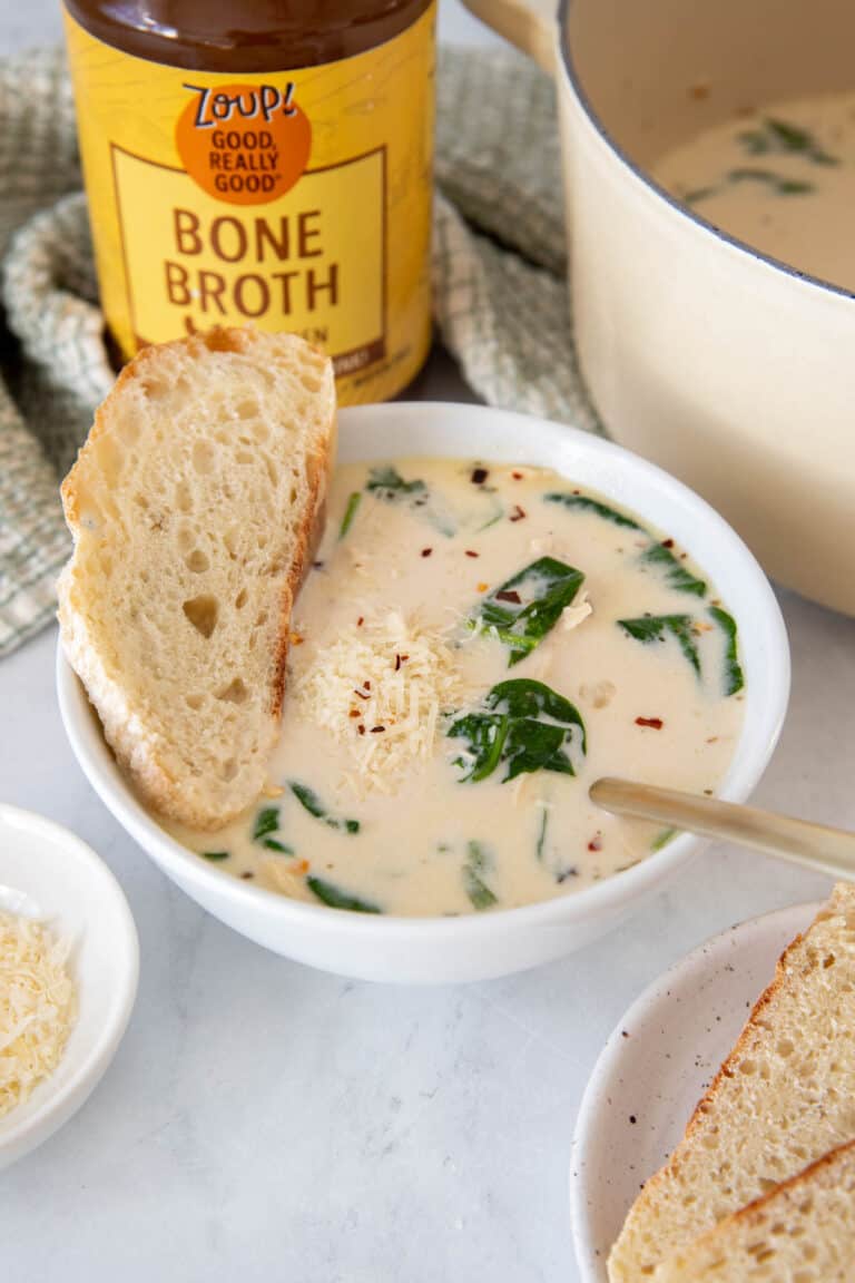 A bowl of chicken florentine soup sitting on a white countertop with a jar of zoup chicken bone broth in the background.