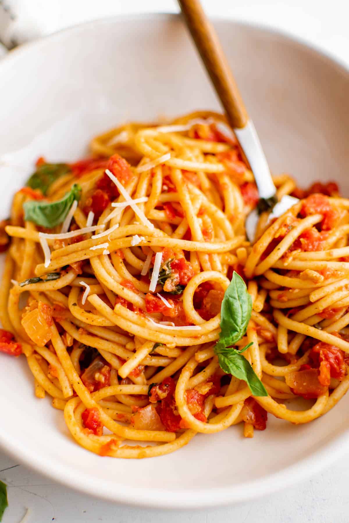 A plate filled with spaghetti arrabbiata and freshly shaved Parmesan cheese. A spoon sits in the dish for eating.