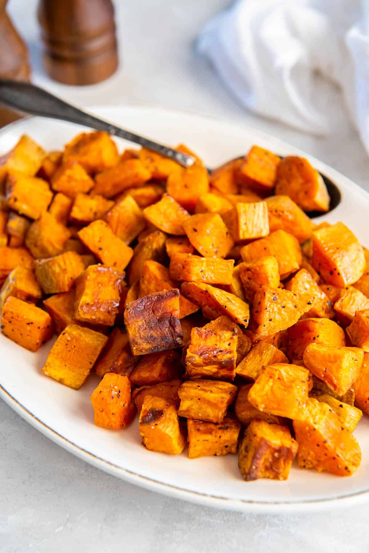 Crispy roasted sweet potatoes on a white plate for serving with a large serving spoon.
