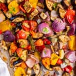 Mediterranean Roasted Vegetables on a sheet pan ready for serving. A spoon scoops up some of the vegetables.