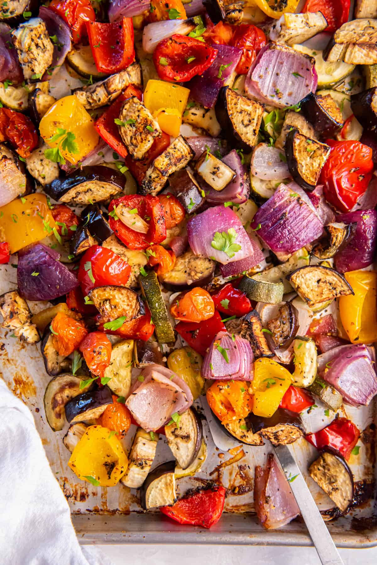 Mediterranean Roasted Vegetables on a sheet pan ready for serving. A spoon scoops up some of the vegetables.