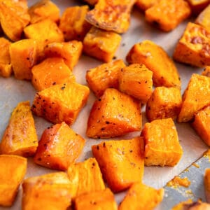 Crispy roasted sweet potatoes cooked on a sheet pan with a spatula for serving.